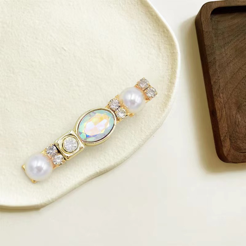 Gold-tone hair clip with pearl-look and iridescent details.